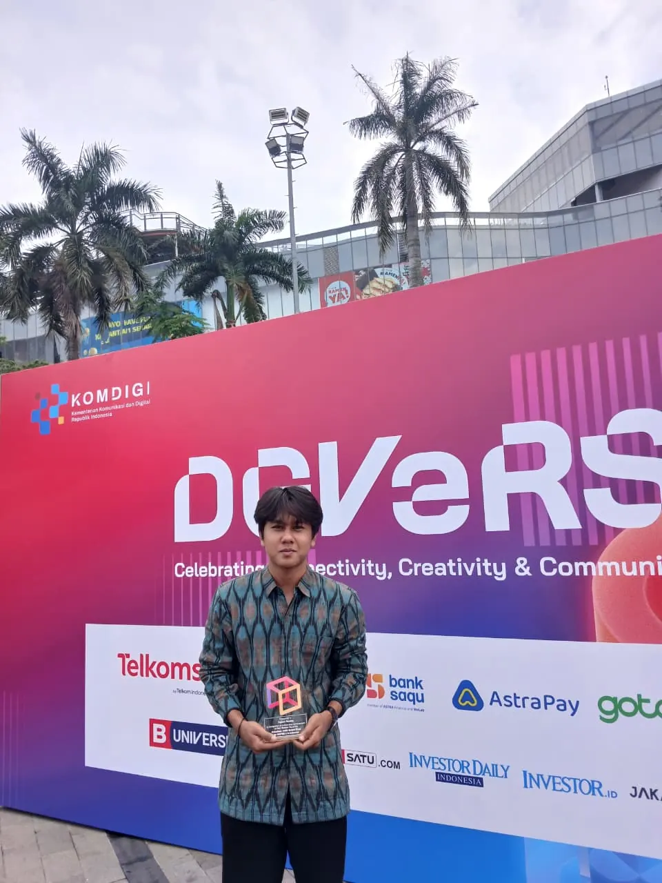 Azril holding a winner's plaque in front of the event backdrop